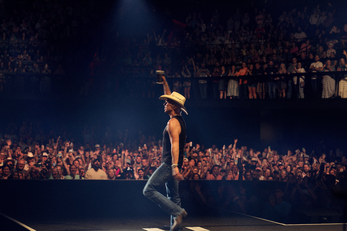Kenny Chesney on stage at The Pinnacle Nashville holding a cup in the air